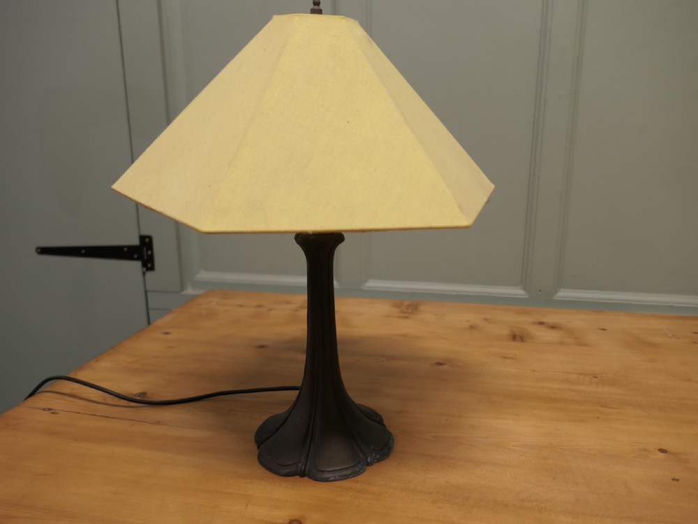 An Art Nouveau table lamp featuring a flared dark metal spelter base and a cream pyramidal fabric shade. View VI