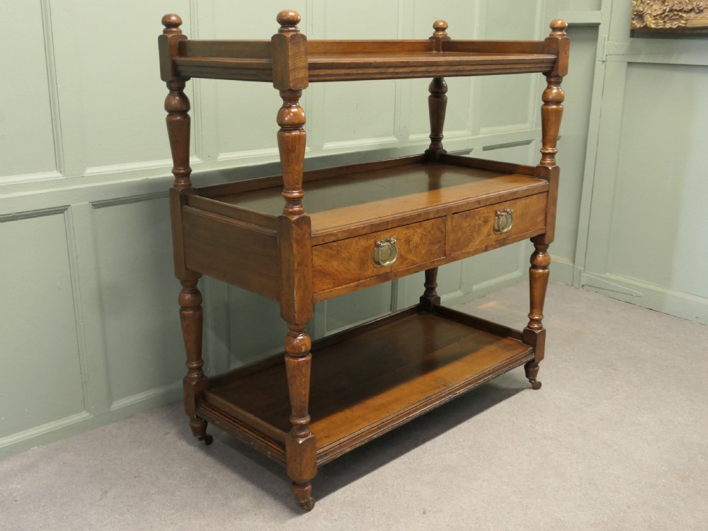 A Victorian oak three-tier buffet featuring turned upright columns, corner finials, two drawers with brass drop handles, and brass castors. View II