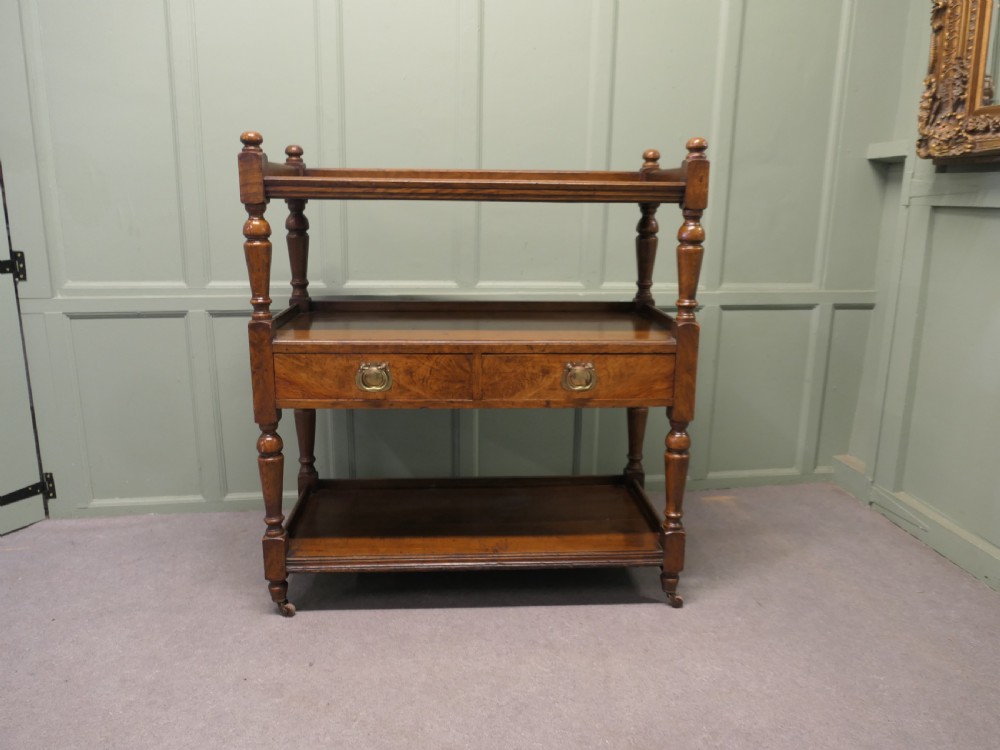 A Victorian oak three-tier buffet featuring turned upright columns, corner finials, two drawers with brass drop handles, and brass castors. View V