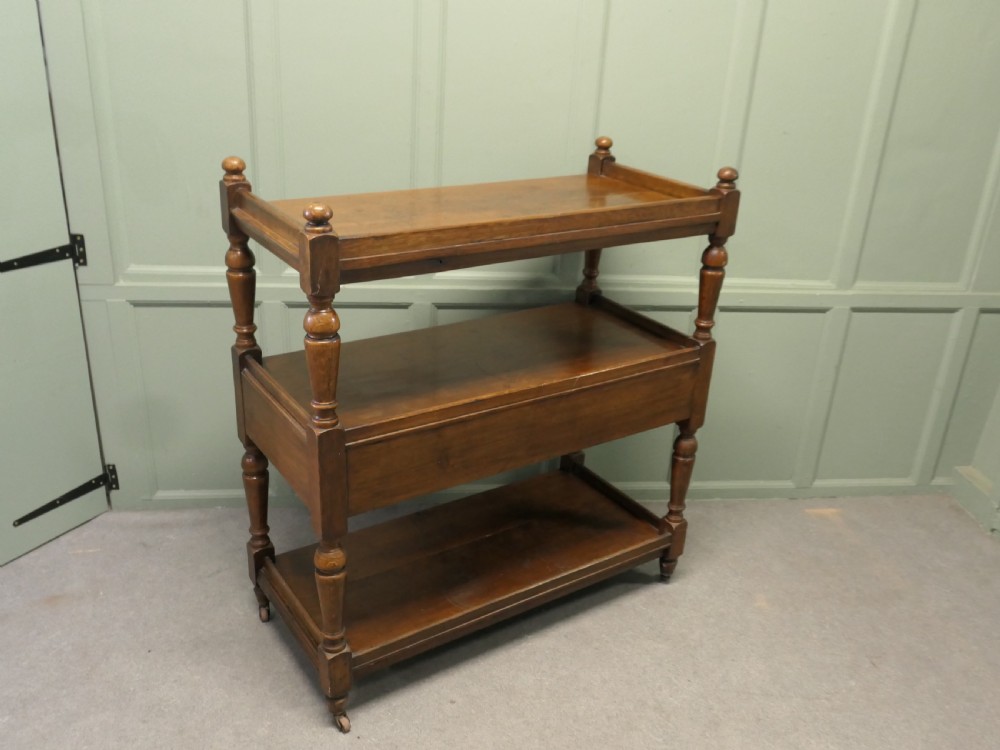 A Victorian oak three-tier buffet featuring turned upright columns, corner finials, two drawers with brass drop handles, and brass castors. View VI