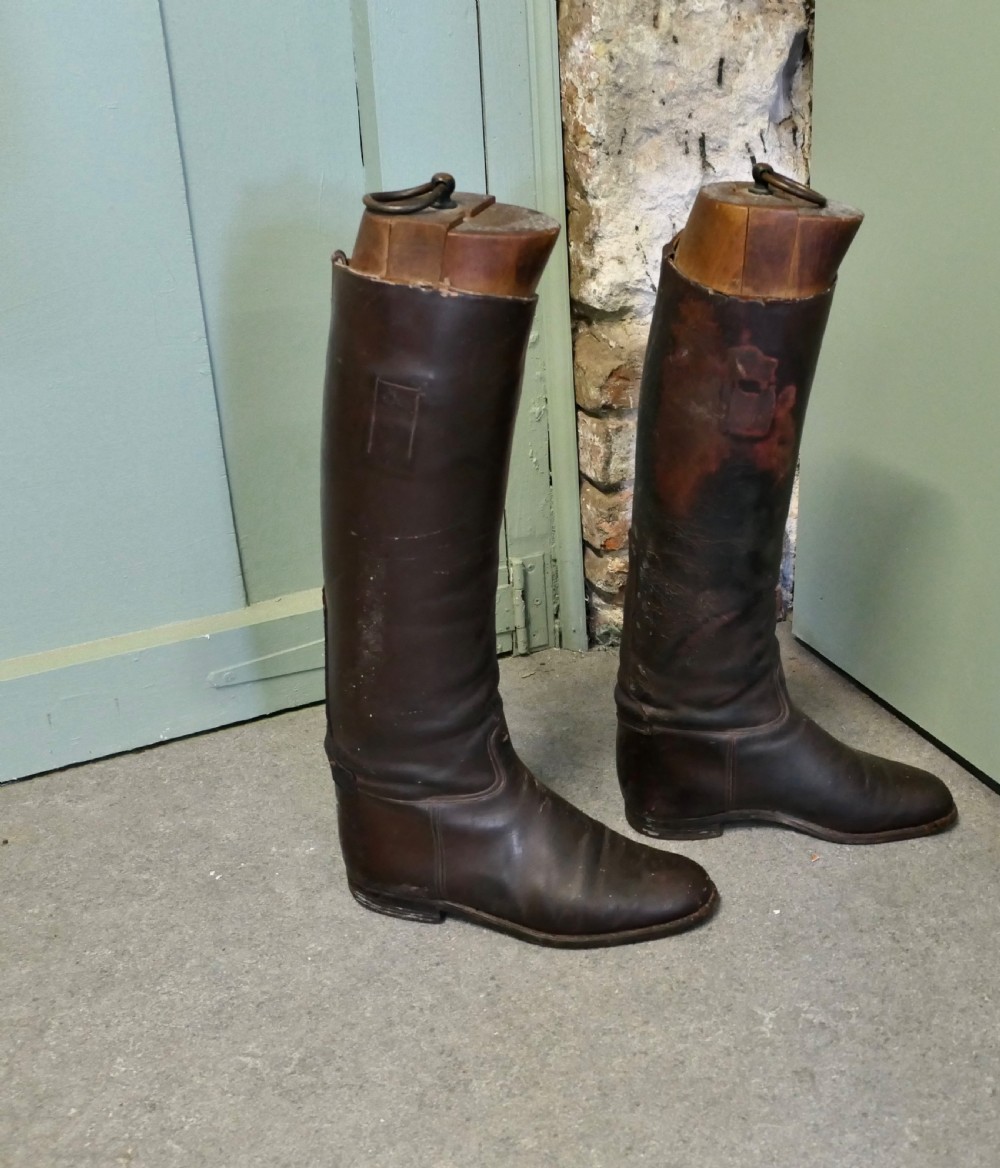 A pair of tall dark brown leather riding boots fitted with carved wooden boot trees featuring metal pull rings. View V