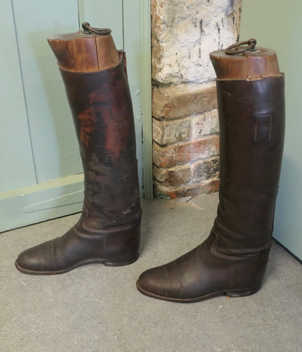 A pair of tall dark brown leather riding boots fitted with carved wooden boot trees featuring metal pull rings. View VI