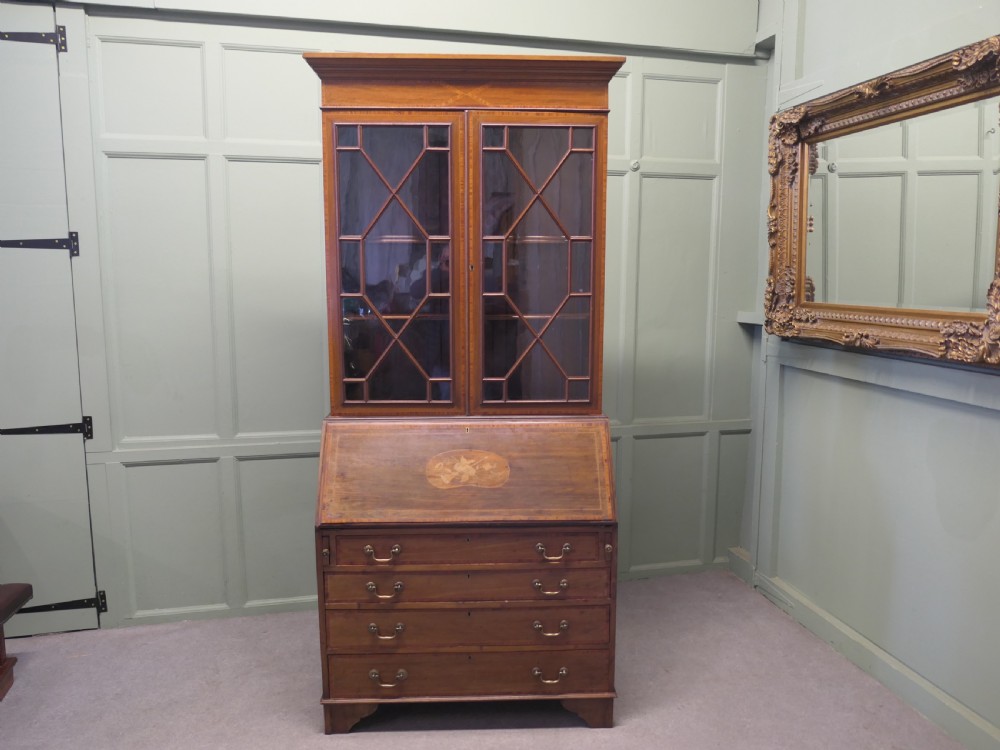An Edwardian mahogany bureau bookcase featuring an upper cabinet with astragal glazed doors, a sloping fall-front writing surface with marquetry inlay, and four lower drawers with brass handles.
