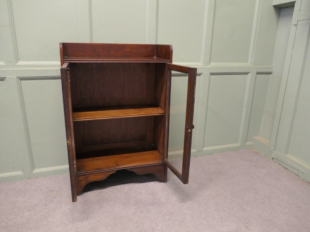 A small dark oak glazed bookcase featuring twin glass panel doors, a raised top gallery, and a shaped lower apron. View VI
