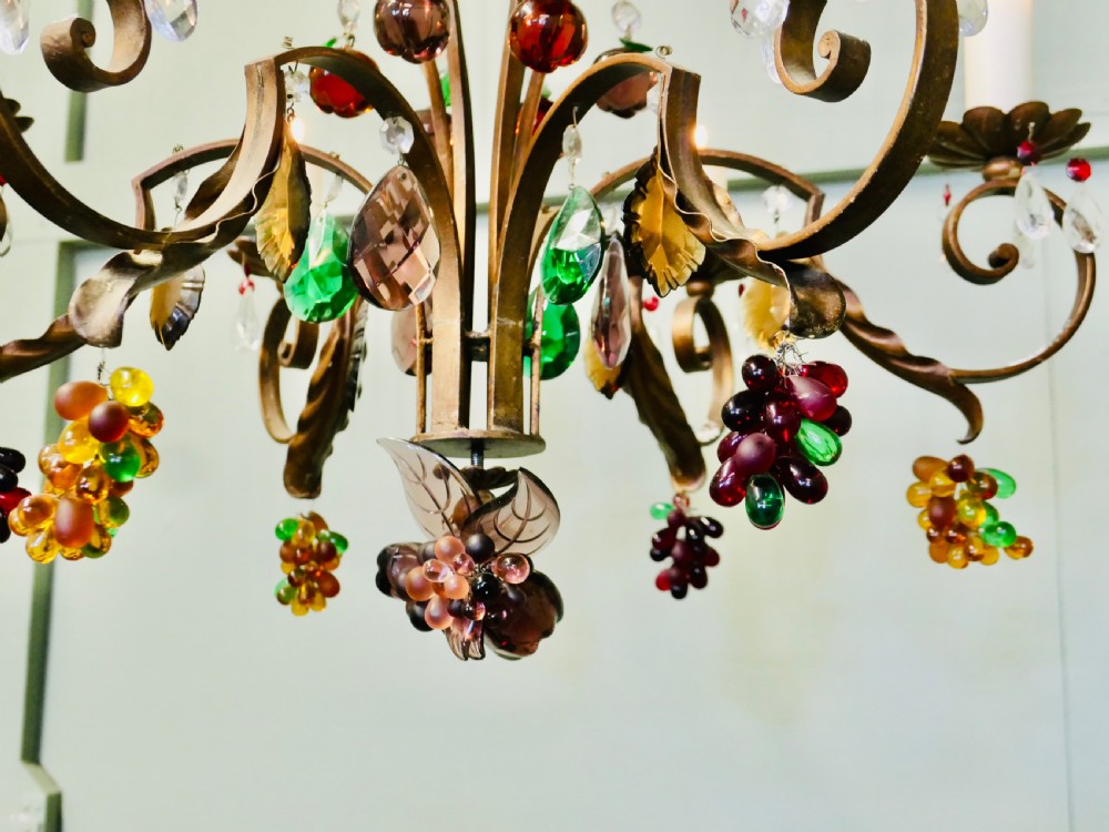 A six-branch wrought iron chandelier decorated with leaf motifs and suspended coloured glass fruit drops, including grapes, apples, and pears. View II