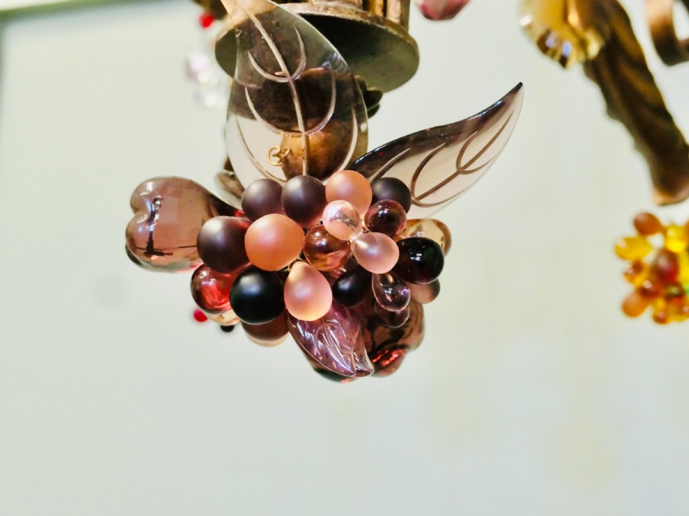 A six-branch wrought iron chandelier decorated with leaf motifs and suspended coloured glass fruit drops, including grapes, apples, and pears. View III