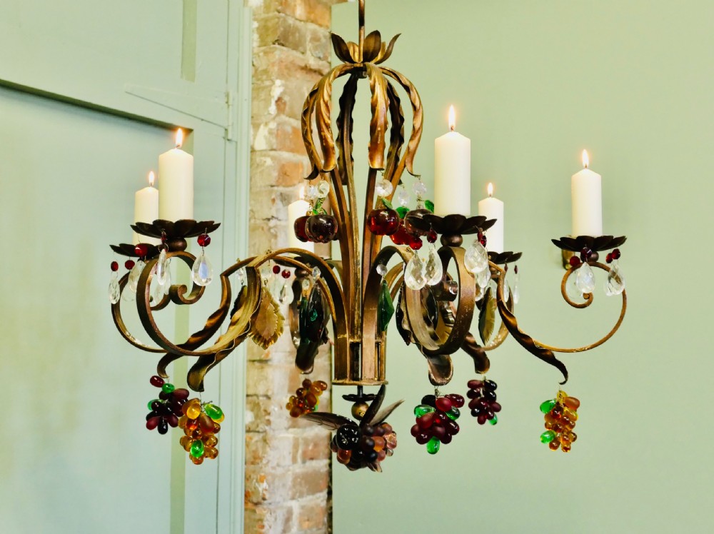 A six-branch wrought iron chandelier decorated with leaf motifs and suspended coloured glass fruit drops, including grapes, apples, and pears. View V