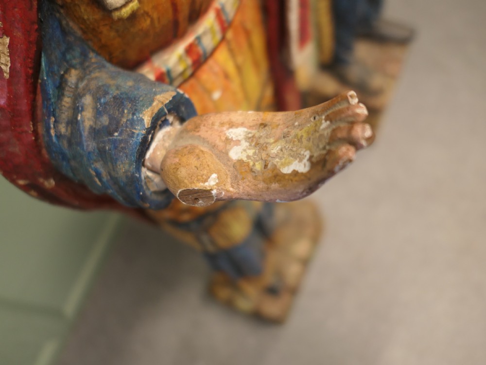 A pair of hand-carved, polychrome painted wooden statues depicting figures in traditional Native American attire set on stone-effect bases. View V