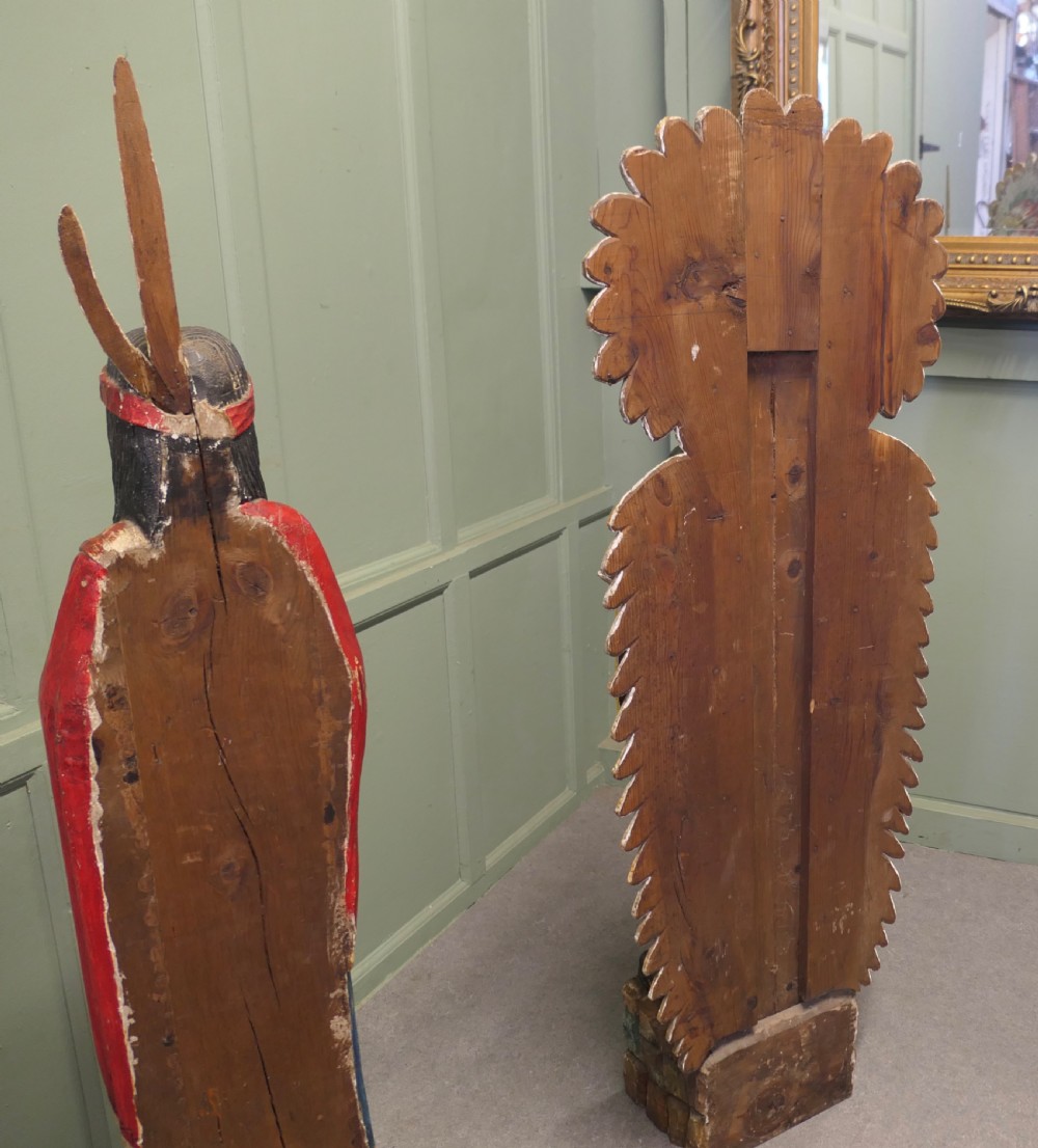A pair of hand-carved, polychrome painted wooden statues depicting figures in traditional Native American attire set on stone-effect bases. View VI