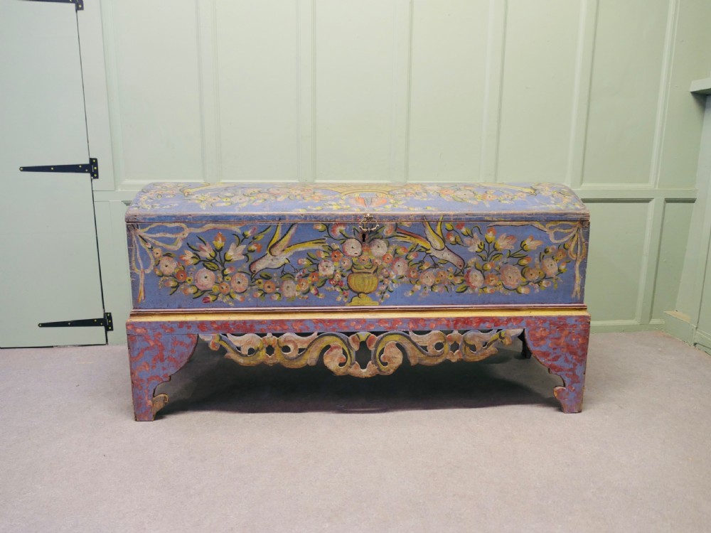 A large blue hand-painted wooden marriage chest decorated with floral motifs, birds, and an openwork scroll-carved base apron.