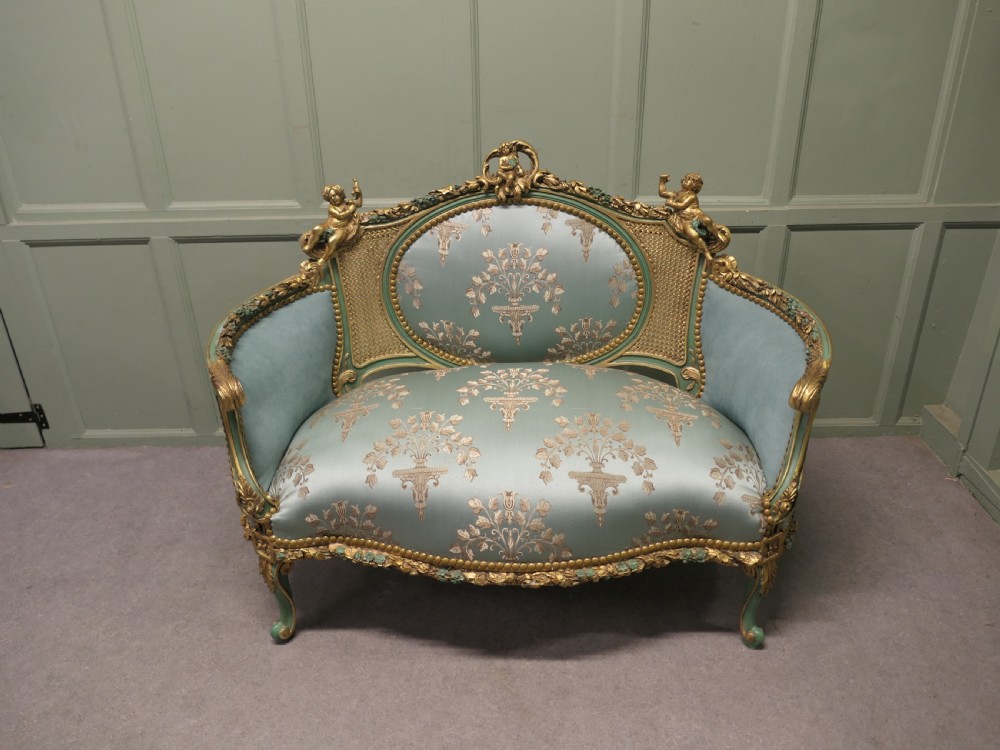 A French Rococo style settee with a green and gold parcel-gilt wooden frame, carved putti cresting, and light green floral silk upholstery.