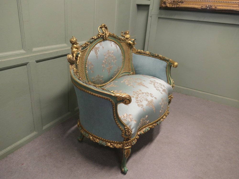A French Rococo style settee with a green and gold parcel-gilt wooden frame, carved putti cresting, and light green floral silk upholstery. View II