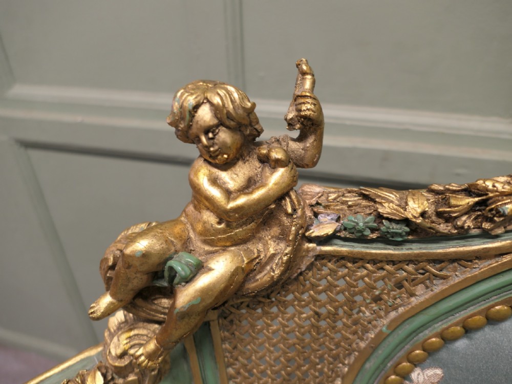 A French Rococo style settee with a green and gold parcel-gilt wooden frame, carved putti cresting, and light green floral silk upholstery. View III