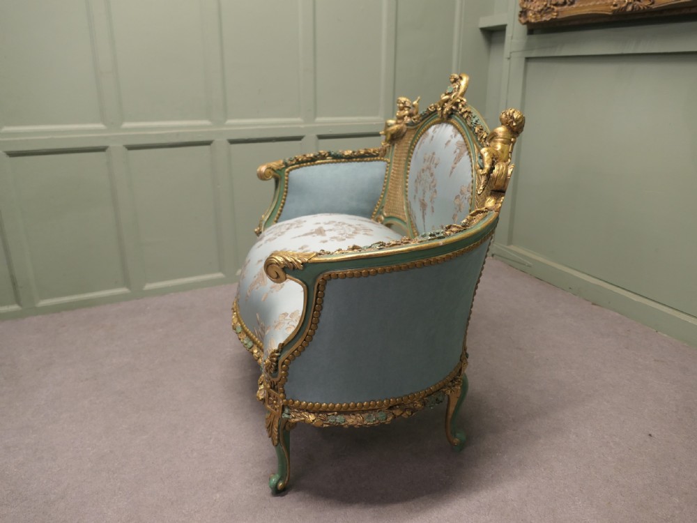 A French Rococo style settee with a green and gold parcel-gilt wooden frame, carved putti cresting, and light green floral silk upholstery. View IV