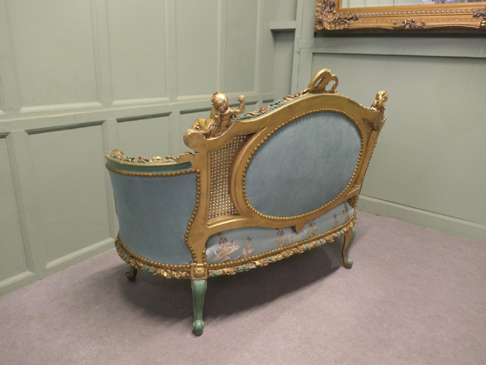 A French Rococo style settee with a green and gold parcel-gilt wooden frame, carved putti cresting, and light green floral silk upholstery. View VI