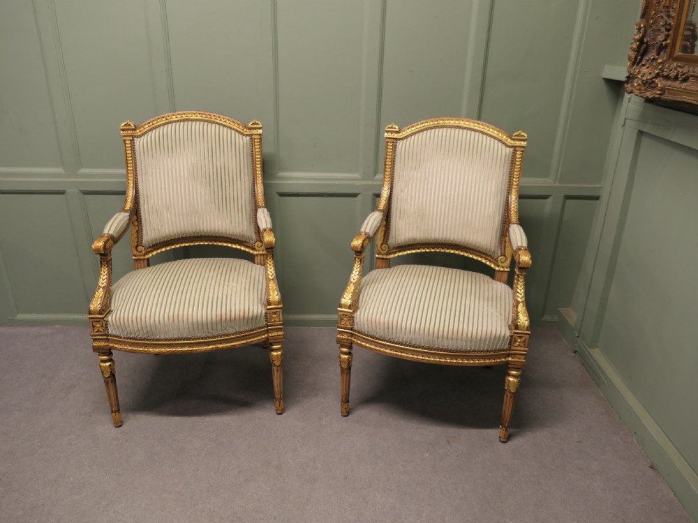 A pair of French style open armchairs featuring carved giltwood frames, fluted legs, and striped sage green and cream fabric upholstery.