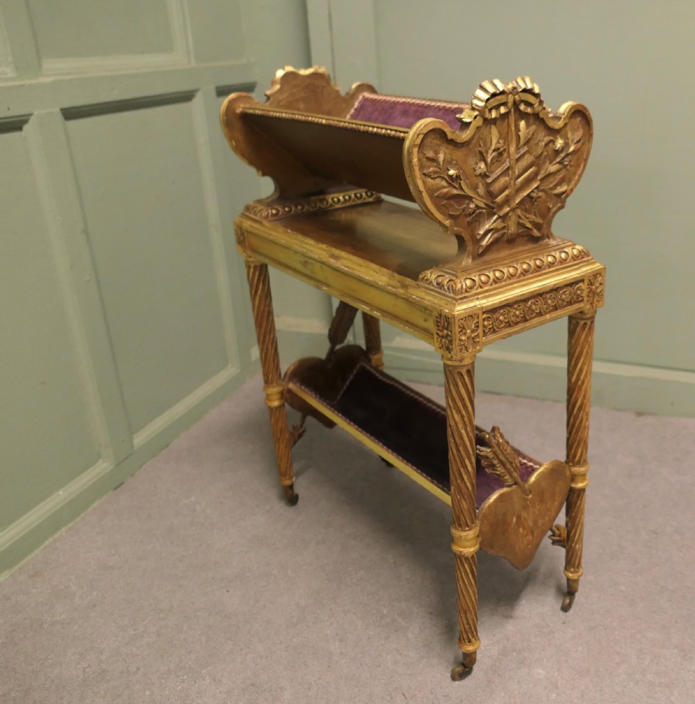 A gilded wooden two-tier book trough featuring spiral legs, carved cresting, and purple velvet lining.