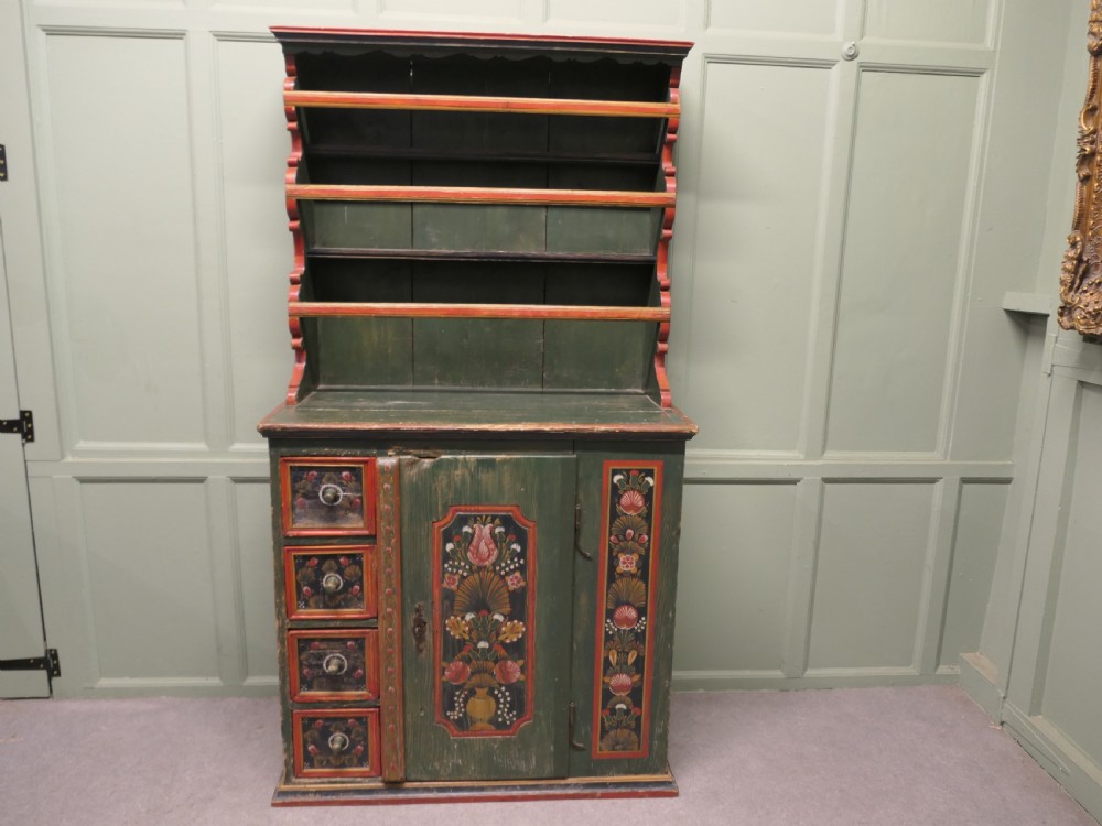 A dark green painted pine folk art dresser featuring an upper open plate rack and hand-painted floral panels on the drawers and lower door.