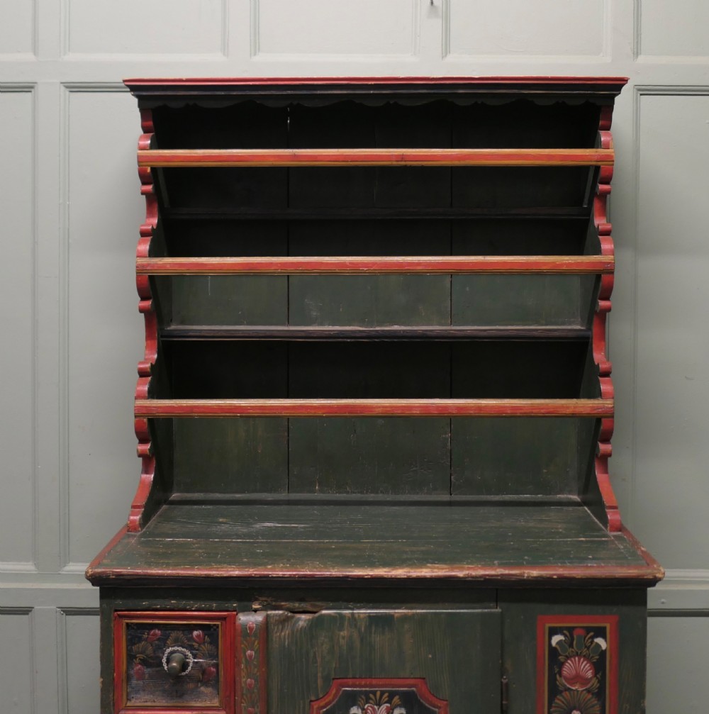 A dark green painted pine folk art dresser featuring an upper open plate rack and hand-painted floral panels on the drawers and lower door. View II