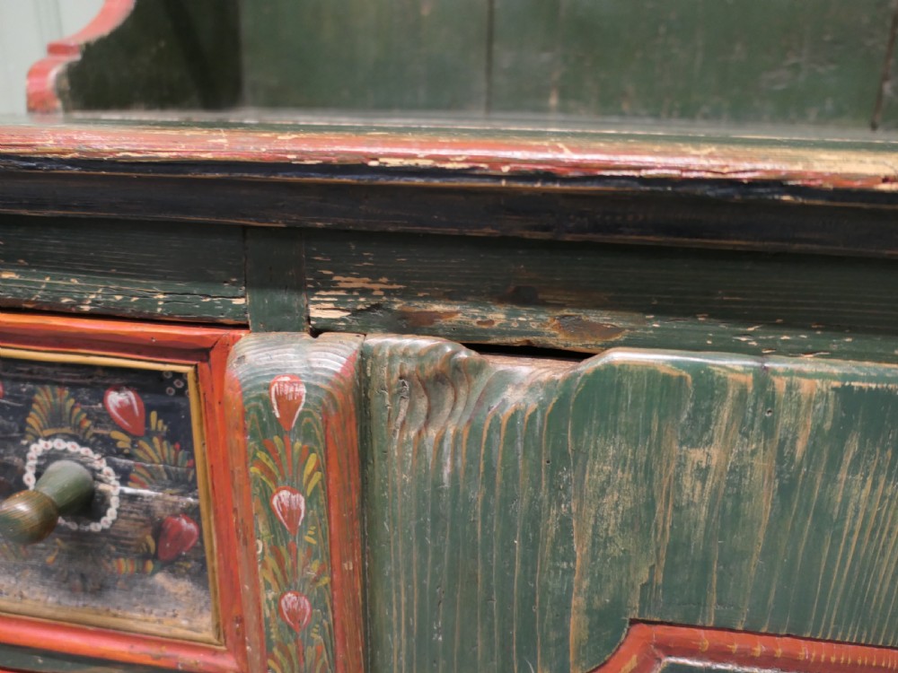 A dark green painted pine folk art dresser featuring an upper open plate rack and hand-painted floral panels on the drawers and lower door. View III