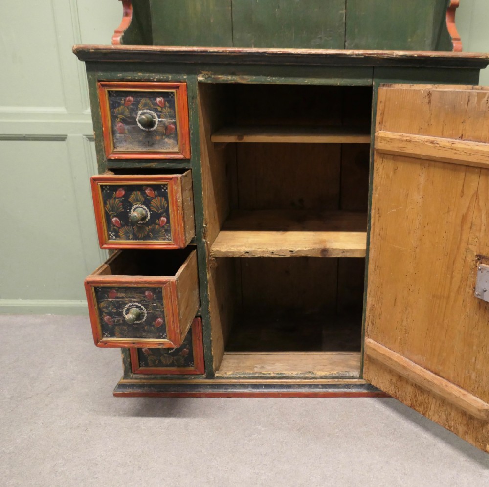 A dark green painted pine folk art dresser featuring an upper open plate rack and hand-painted floral panels on the drawers and lower door. View VI