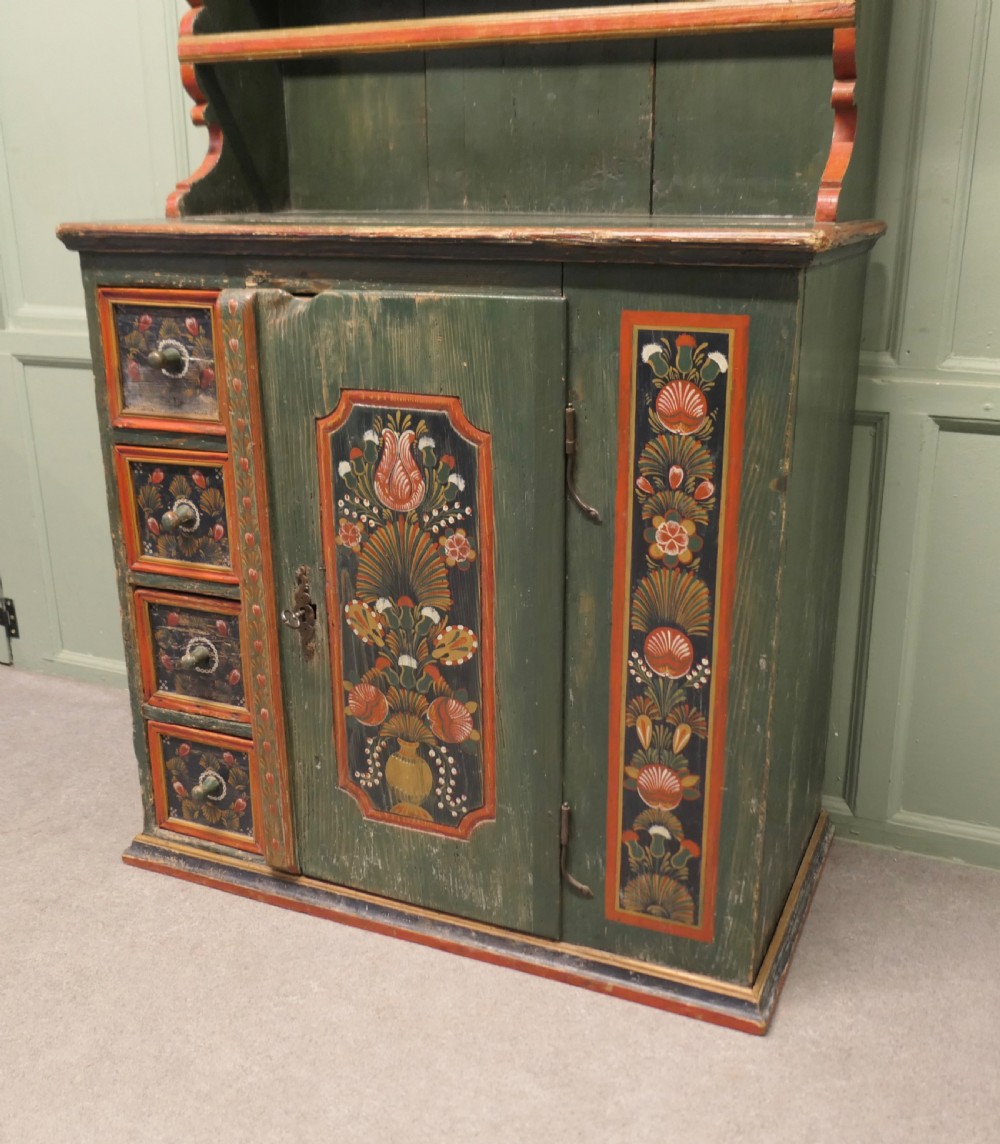 A dark green painted pine folk art dresser featuring an upper open plate rack and hand-painted floral panels on the drawers and lower door. View VII