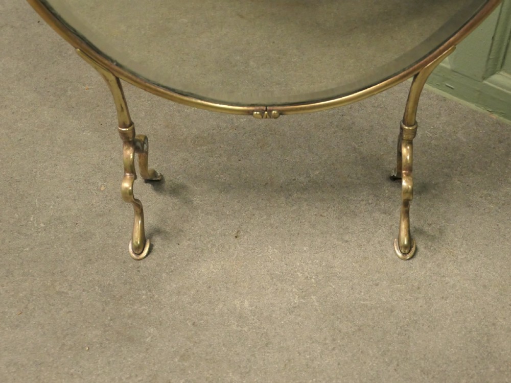 An Art Nouveau brass fire screen featuring a circular mirror frame topped with an intricate whiplash crest and resting on two curved metal legs. View III