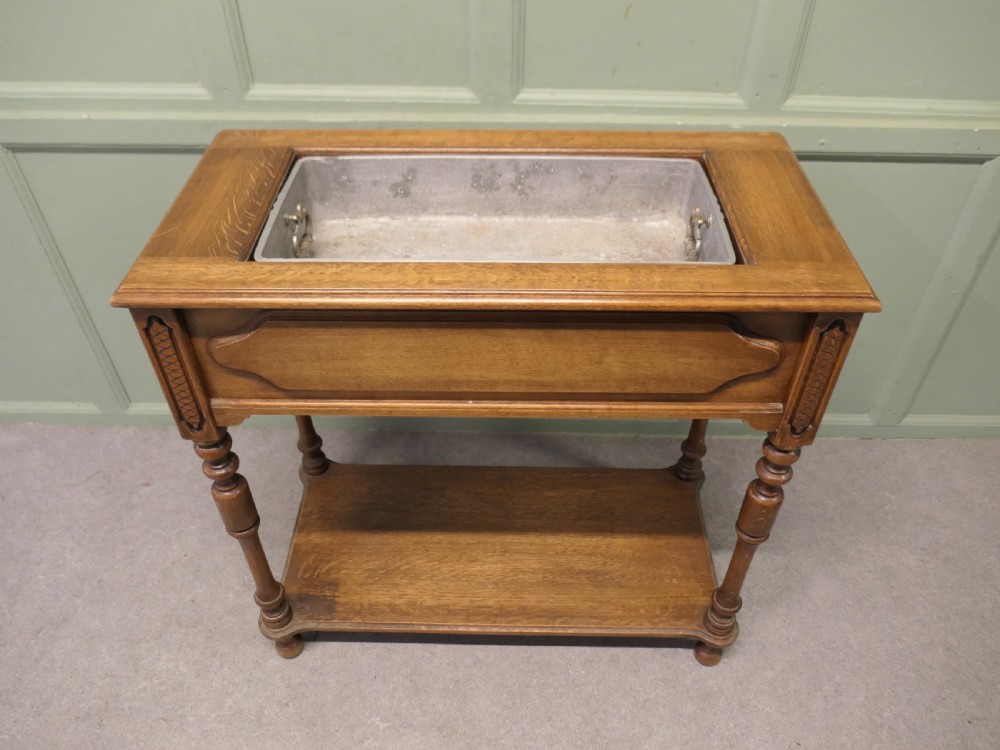 A French Arts and Crafts golden oak jardiniere stand featuring a recessed metal trough liner, carved corner detailing, turned legs, and a lower shelf.