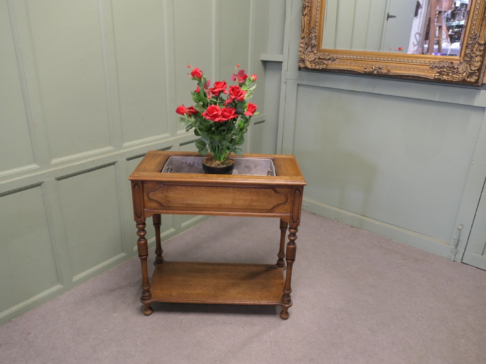 A French Arts and Crafts golden oak jardiniere stand featuring a recessed metal trough liner, carved corner detailing, turned legs, and a lower shelf. View II