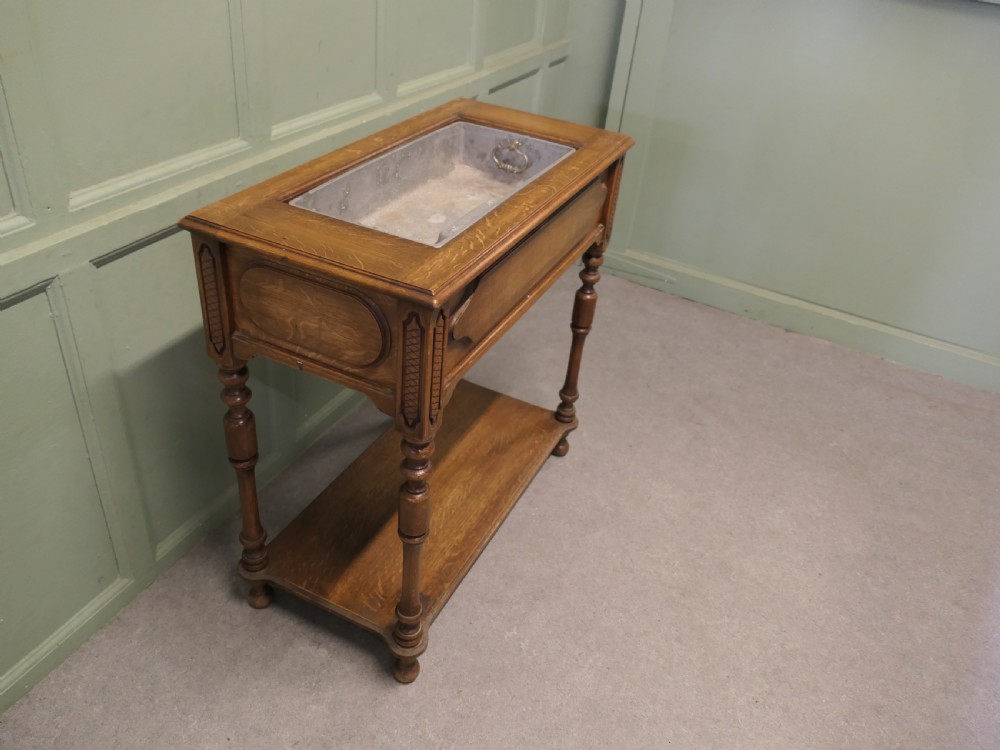 A French Arts and Crafts golden oak jardiniere stand featuring a recessed metal trough liner, carved corner detailing, turned legs, and a lower shelf. View IV