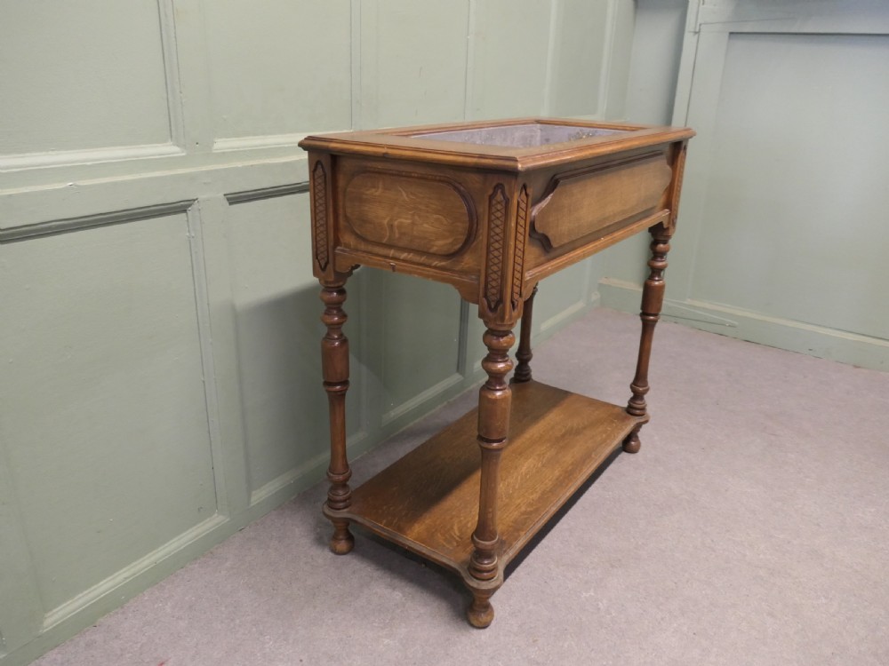 A French Arts and Crafts golden oak jardiniere stand featuring a recessed metal trough liner, carved corner detailing, turned legs, and a lower shelf. View VI