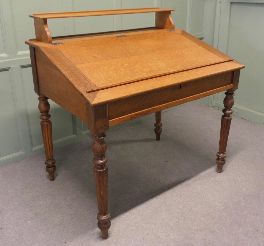 An antique French oak clerks desk featuring a slanted hinged writing surface, a upper gallery shelf, and four turned legs.