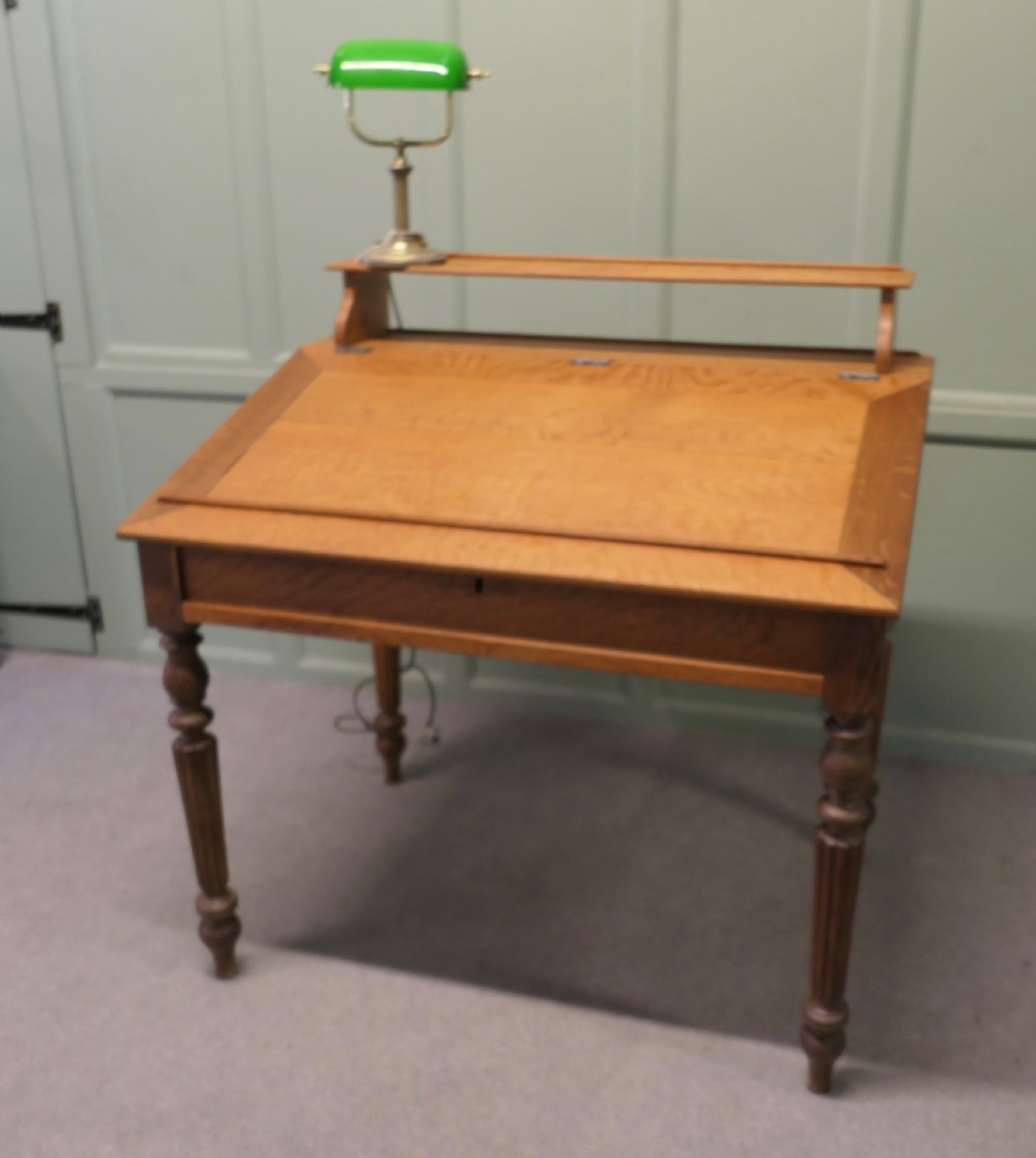 An antique French oak clerks desk featuring a slanted hinged writing surface, a upper gallery shelf, and four turned legs. View II