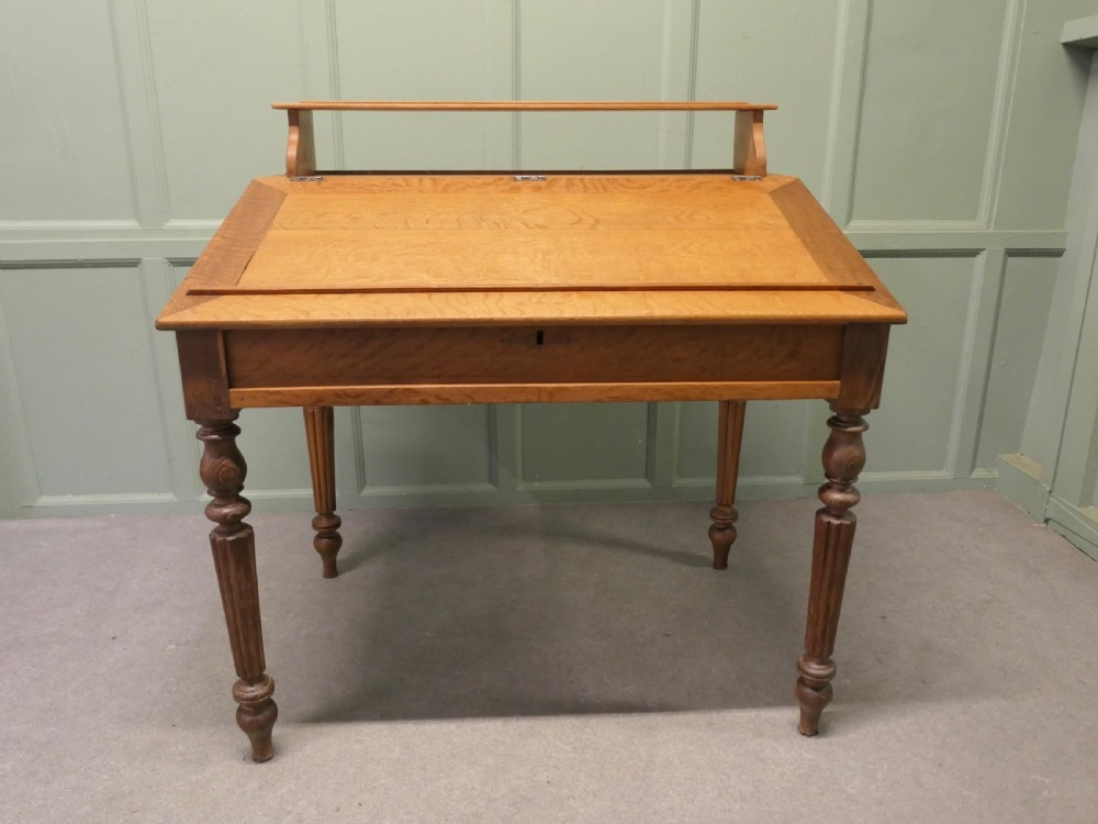 An antique French oak clerks desk featuring a slanted hinged writing surface, a upper gallery shelf, and four turned legs. View III