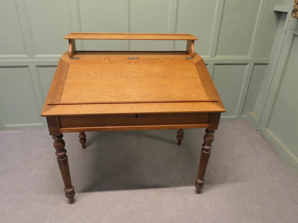 An antique French oak clerks desk featuring a slanted hinged writing surface, a upper gallery shelf, and four turned legs. View VI