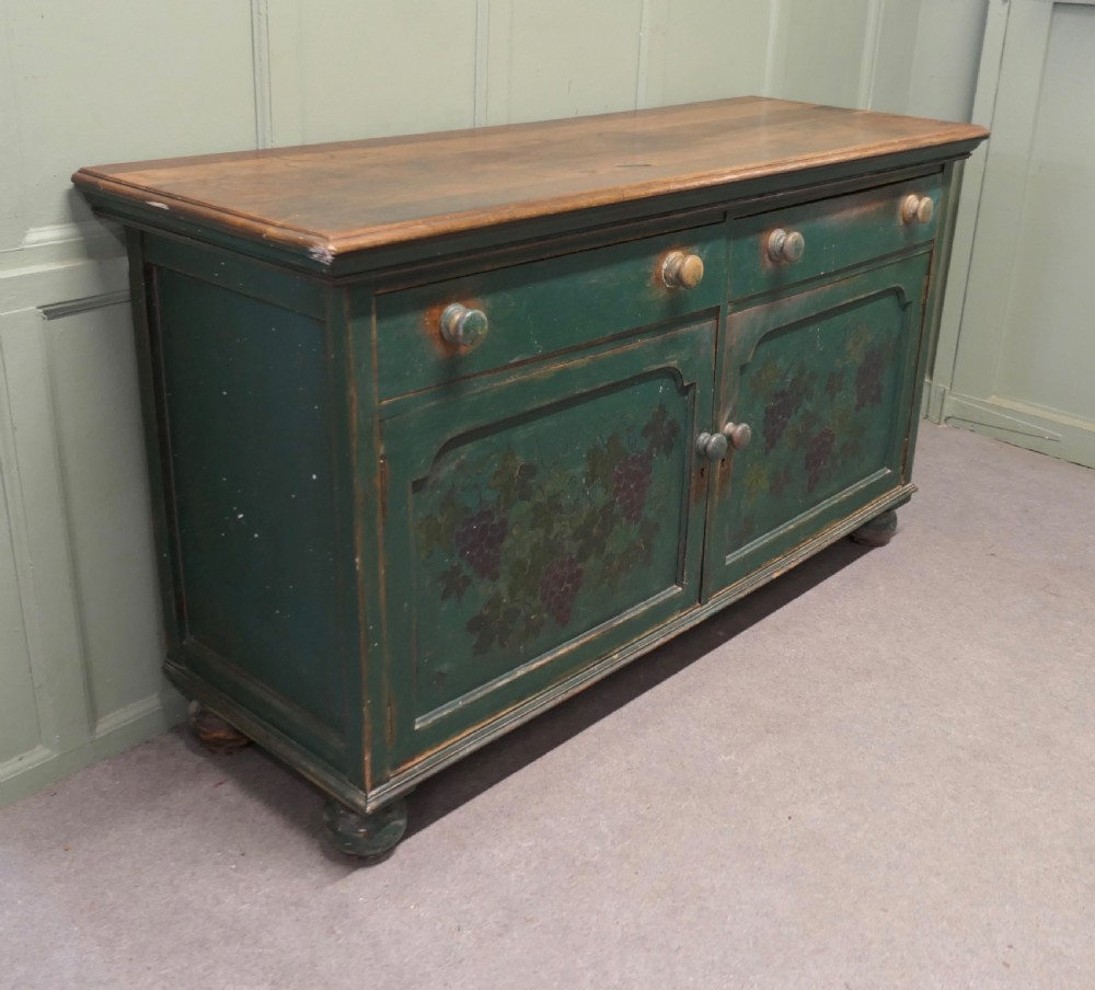 A Victorian green painted wooden dresser base with two drawers, two lower cabinet doors featuring hand-painted grape motifs, and a natural wood top surface. View II