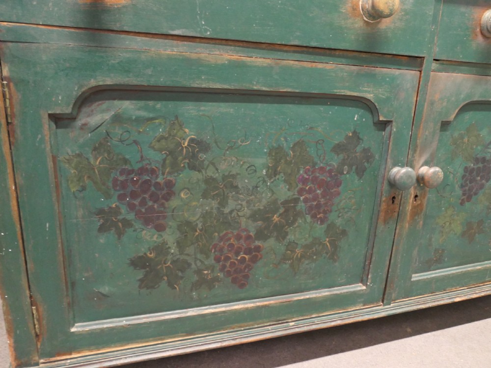 A Victorian green painted wooden dresser base with two drawers, two lower cabinet doors featuring hand-painted grape motifs, and a natural wood top surface. View V