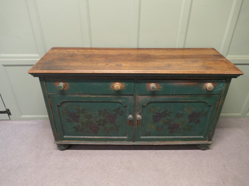 A Victorian green painted wooden dresser base with two drawers, two lower cabinet doors featuring hand-painted grape motifs, and a natural wood top surface. View VI
