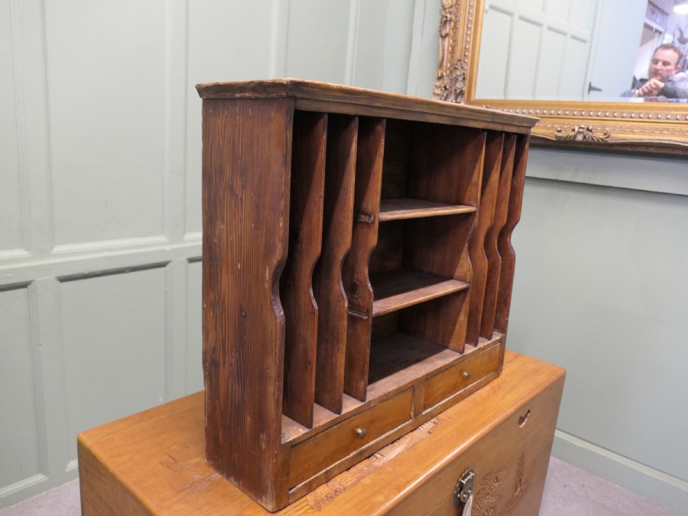 A warm brown wooden desk organiser with vertical document slots, central shelves, and two small drawers at the base. View III