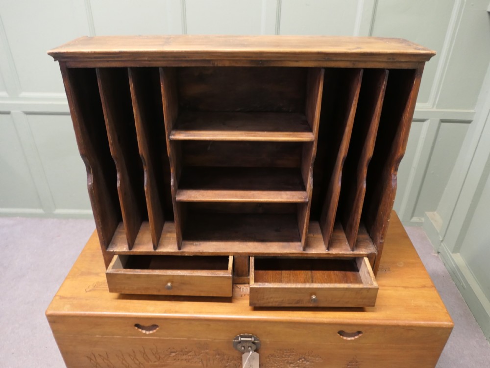 A warm brown wooden desk organiser with vertical document slots, central shelves, and two small drawers at the base. View IV