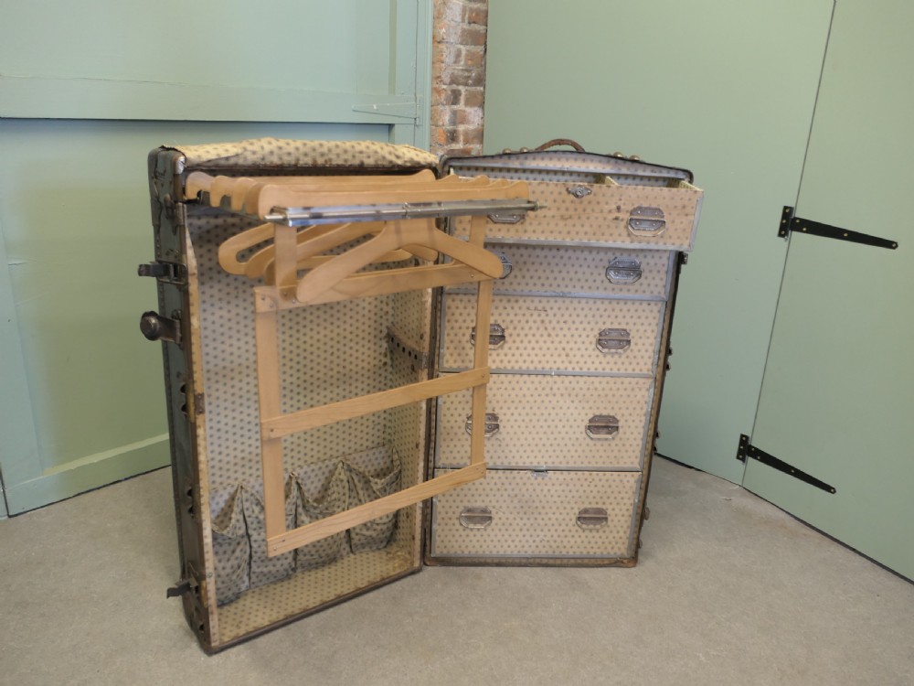 An upright dark brown metal-bound fitted steamer trunk wardrobe featuring riveted corners and heavy brass latches. View III