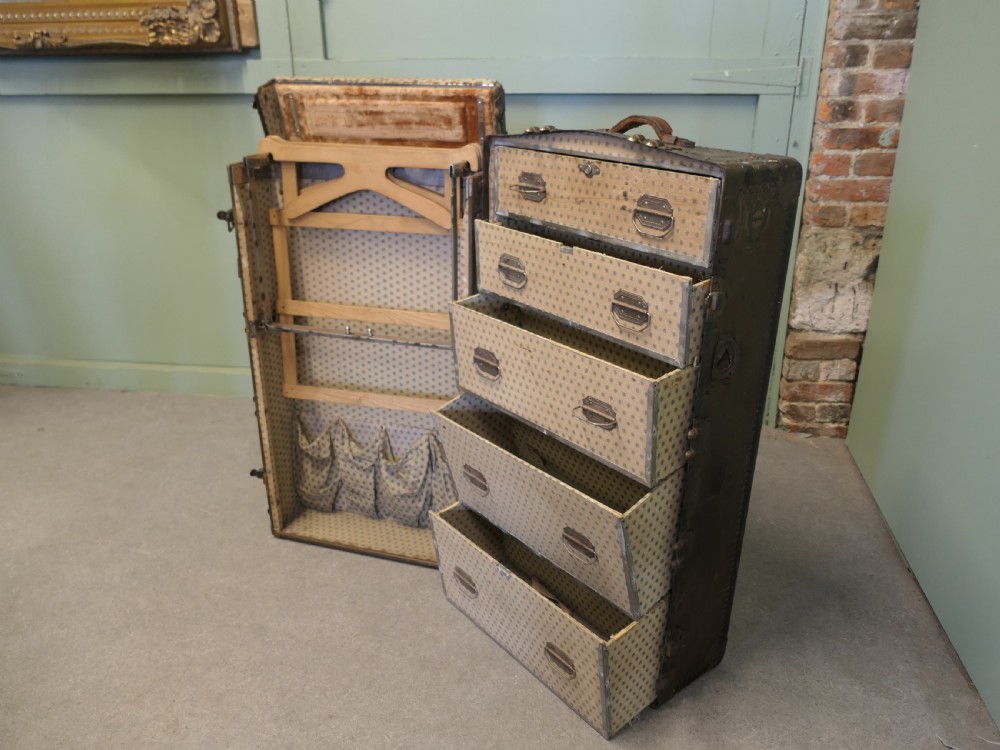 An upright dark brown metal-bound fitted steamer trunk wardrobe featuring riveted corners and heavy brass latches. View IV