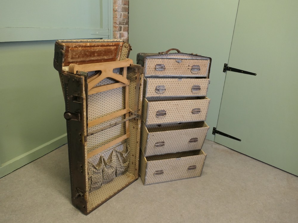 An upright dark brown metal-bound fitted steamer trunk wardrobe featuring riveted corners and heavy brass latches. View V