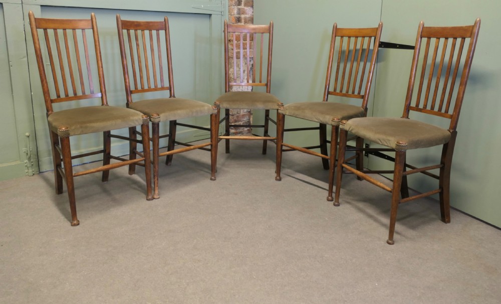 Set of five Arts and Crafts golden oak dining chairs featuring vertical slat backrests and fabric upholstered seats.