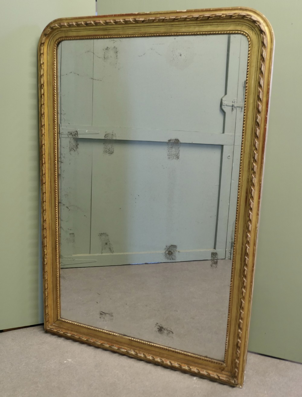 A large 19th-century French Louis Philippe wall mirror featuring a gilded frame with rounded upper corners, beaded inner border, and foxed mirror glass.