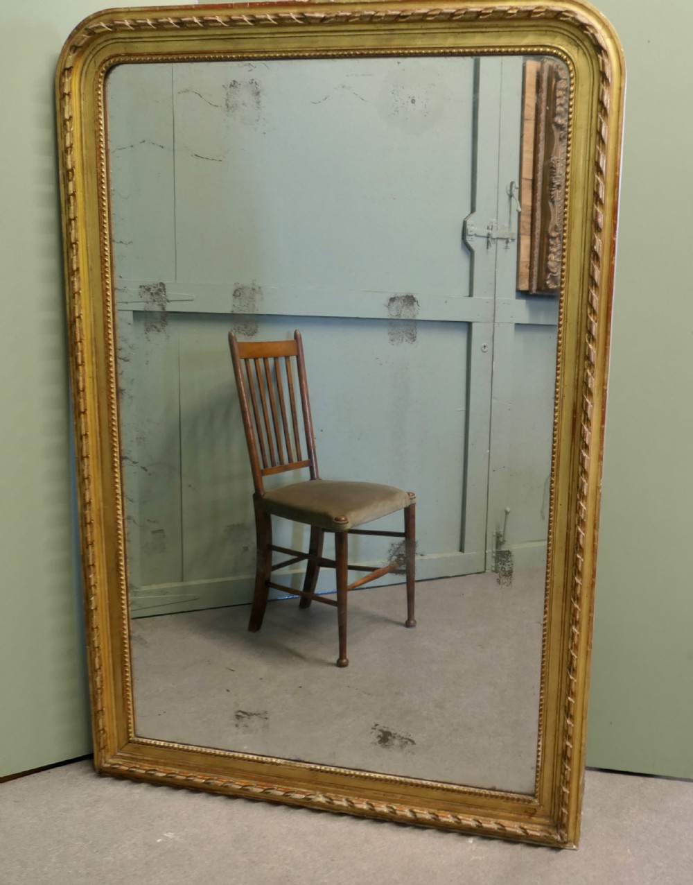 A large 19th-century French Louis Philippe wall mirror featuring a gilded frame with rounded upper corners, beaded inner border, and foxed mirror glass. View II
