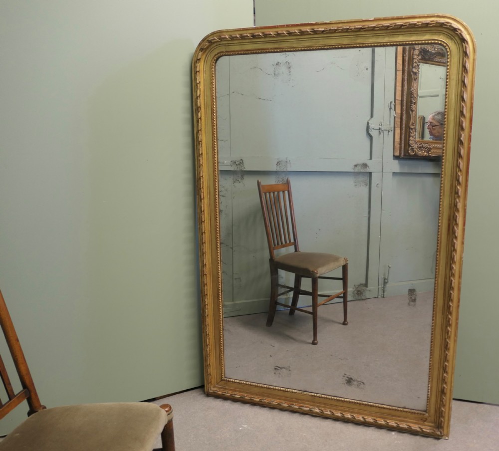 A large 19th-century French Louis Philippe wall mirror featuring a gilded frame with rounded upper corners, beaded inner border, and foxed mirror glass. View IV