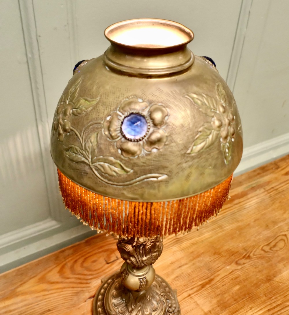 A French Arts and Crafts brass reading lamp featuring a dome shade adorned with floral repousse work, blue glass cabochons, and beaded fringe on a sculpted stem. View VI