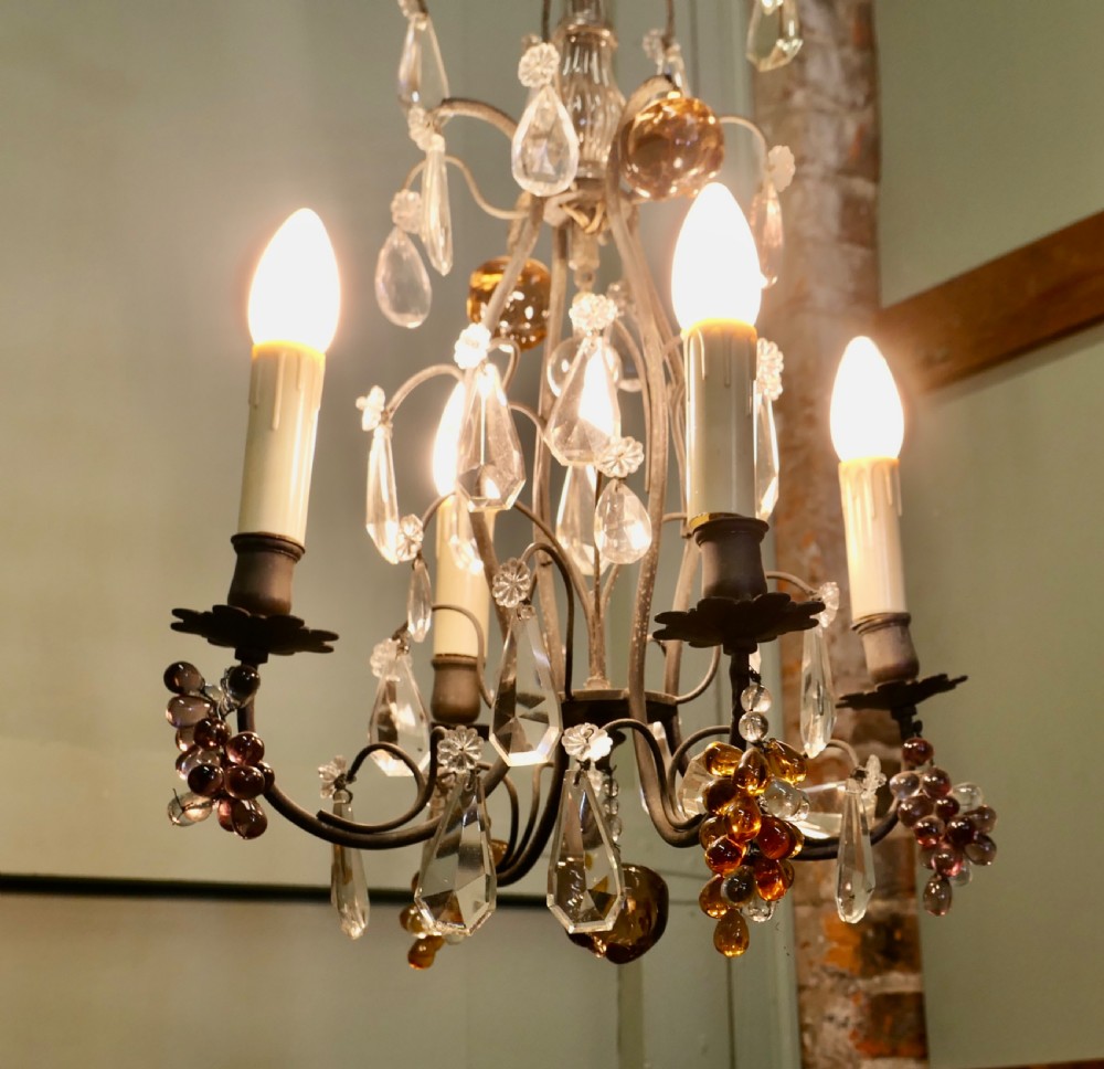 A French metal chandelier featuring scroll arms, electric candle sleeves, clear crystal droplets, and coloured glass fruit ornaments in amber and mauve tones. View III