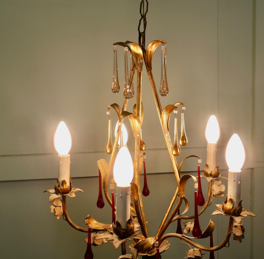 A French gilt metal chandelier featuring five curved candle arms decorated with leaf foliage and hung with clear, amber, and red glass teardrops. View III
